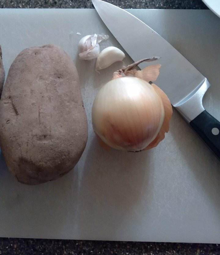image of potato, onion, and garlic and knife for easy breakfast potatoes recipe.